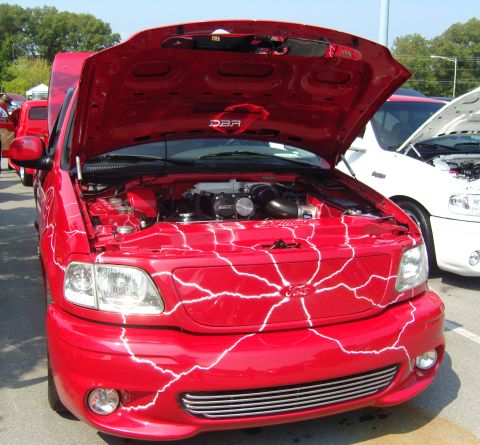 2007 Ford Mustang - A red 1999 Ford F-150 Lightning pickup truck with custom graphics and its hood open is parked next to another vehicle.