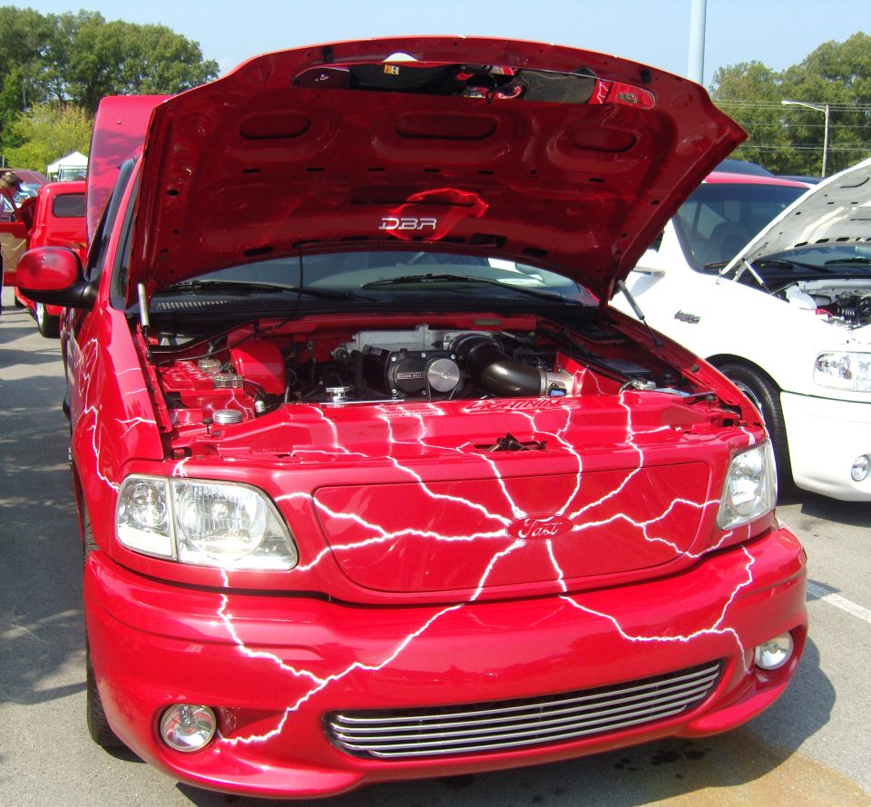 Red Ford F-150 Lightning pickup truck with white lightning bolt graphics and chrome grille, hood open