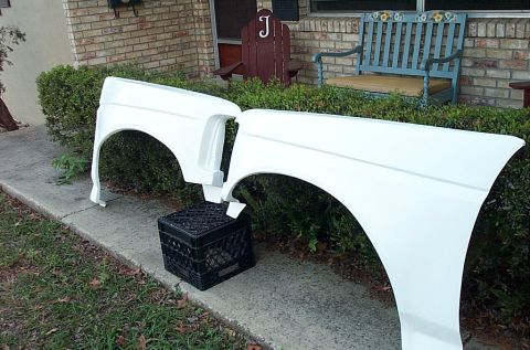 1995 Ford Bronco - A pair of white fiberglass front fenders propped on a black milk crate and a hedge along a concrete walkway outside a brick house, showing…