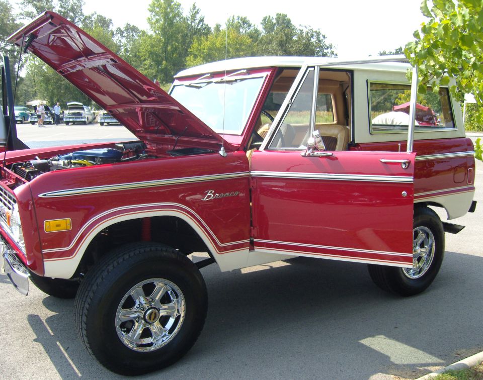 Red Ford Bronco with white top, hood and driver door open. Chrome wheels