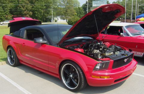 2007 Ford Mustang - A red Ford Mustang with its hood up is parked next to another classic Mustang.