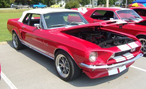 2007 Ford Mustang - A red 1967 Ford Mustang convertible with its hood open is parked next to another red Mustang at an outdoor car show.