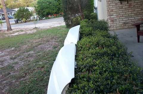 1995 Ford Bronco - Two white removable fiberglass roof panels or body panels leaned upright against a hedge alongside a brick house, resting on the grass betw…