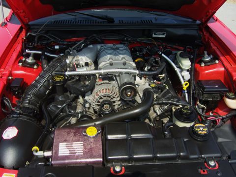 2007 Ford Mustang - The engine bay of a red vehicle, likely a Ford Mustang from the early 2000s, is shown with a prominent supercharger.