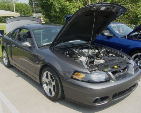 2007 Ford Mustang - A gray 2007 Ford Mustang is displayed with its hood open, revealing the engine compartment. Another blue vehicle is visible in the backgrou…