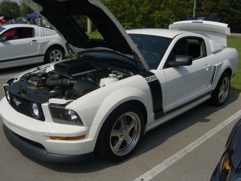 2007 Ford Mustang - A white Ford Mustang with a BOSS 302 decal on the fender and hood open, parked next to another Mustang.