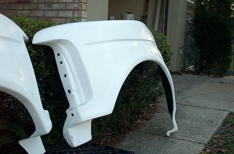 1995 Ford Bronco - Close view of a white fiberglass front fender with a squared wheel opening and a row of mounting holes along its inner edge, standing uprig…