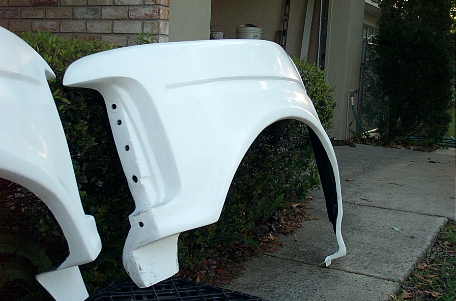White fiberglass truck front fender standing upright beside a brick house walkway