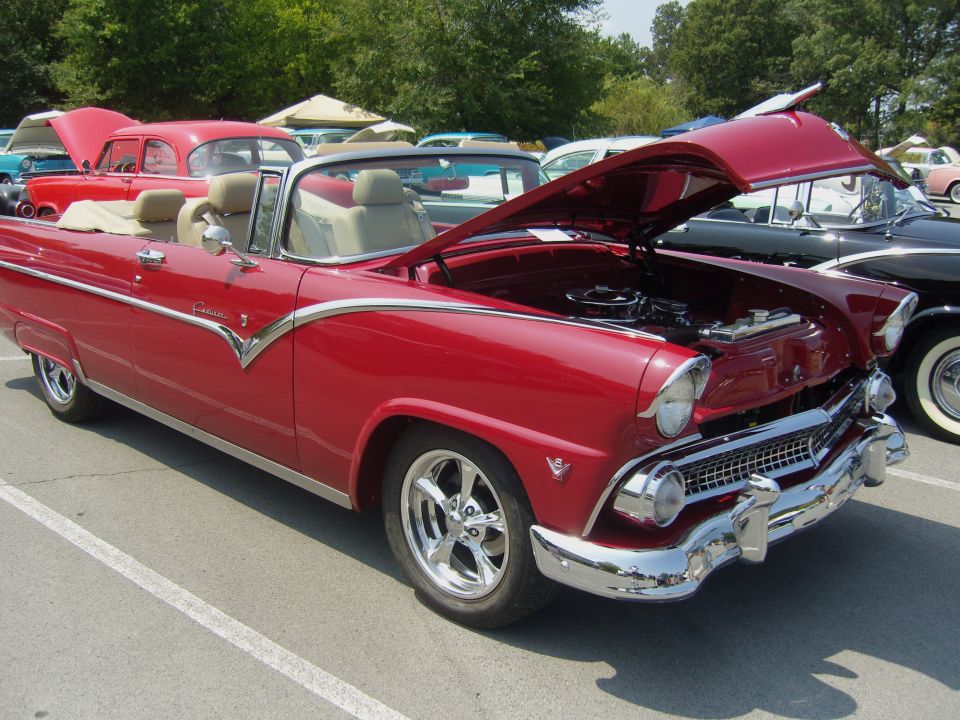 Red convertible classic car with hood open, parked at an outdoor car show