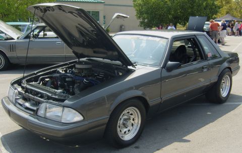 2007 Ford Mustang - A dark gray Ford Mustang Fox Body is parked with its hood open, revealing the engine compartment.