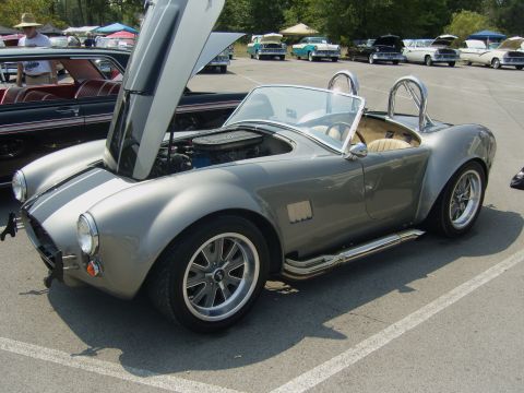 2007 Ford Mustang - A gray AC Cobra roadster is parked with its hood open, revealing the engine bay.