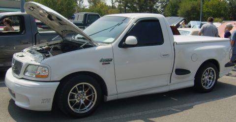 2007 Ford Mustang - A white 1999 Ford F-150 SVT Lightning pickup truck is parked outdoors with its hood open, displaying its engine.
