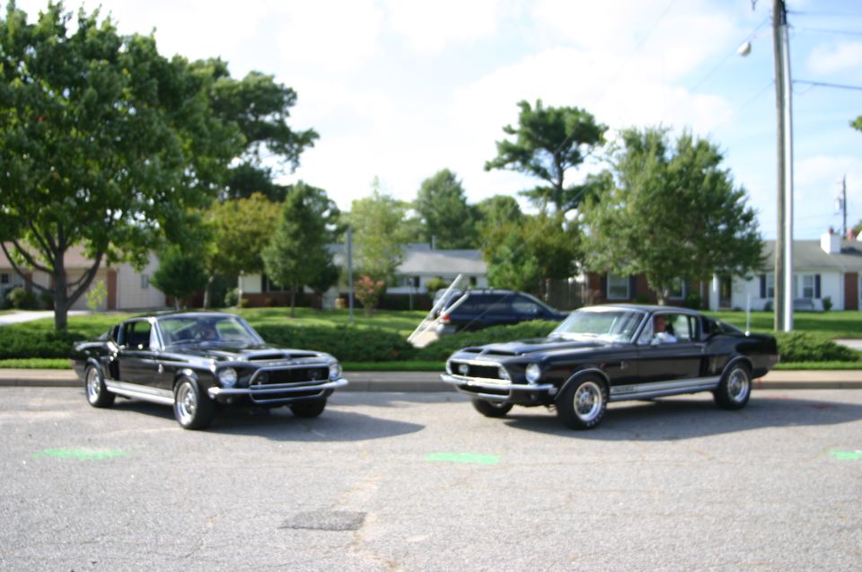 Two black 1968 Shelby GT500s parked side-by-side