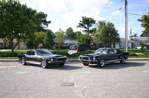 1968 Shelby GT500 - Two black 1968 Ford Mustangs are parked in a lot on a sunny day.