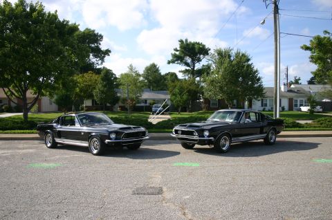 1968 Shelby GT500 - Two black 1968 Shelby GT500s are parked on a street in front of houses.