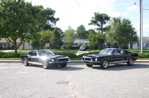 1968 Shelby GT500 - Two black 1968 Shelby GT500 Mustangs are parked on asphalt with houses and trees in the background.
