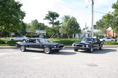 1968 Shelby GT500 - Two black 1968 Shelby GT500 Mustangs are parked on a street, with houses and trees in the background.