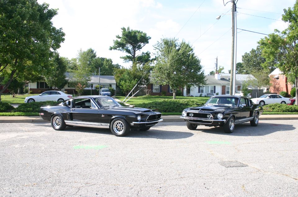 Two black 1968 Shelby GT500 Mustangs parked side-by-side