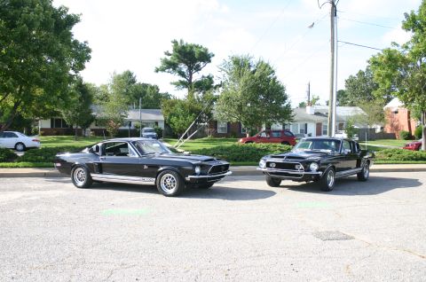 1968 Shelby GT500 - Two black 1968 Shelby GT500 Mustangs are parked on a street in front of houses.