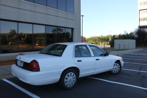 2003 Ford Crown Victoria - A white 2003 Ford Crown Victoria is parked in a lot next to a modern office building.