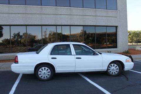 2003 Ford Crown Victoria - Side profile of a white 2003 Ford Crown Victoria parked in front of a modern building.