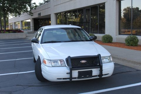 2003 Ford Crown Victoria - A white Ford Crown Victoria police car is parked in a lot in front of an office building.