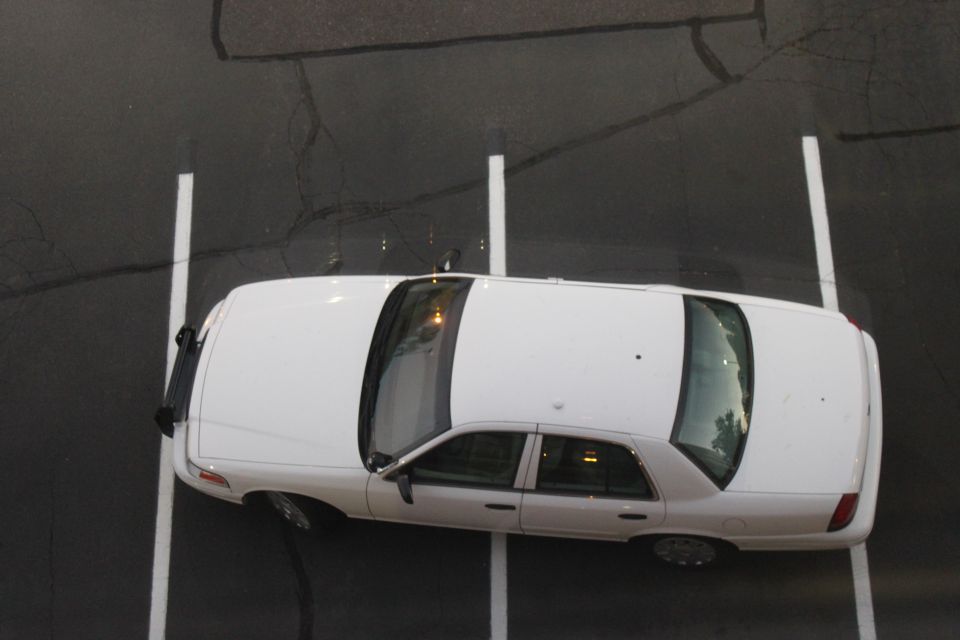 Overhead top-down view of a white four-door sedan parked in a marked parking stall