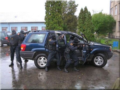1991 Ford Crown Victoria - Police officers conduct a raid, exiting a blue Jeep Grand Cherokee on a wet day.