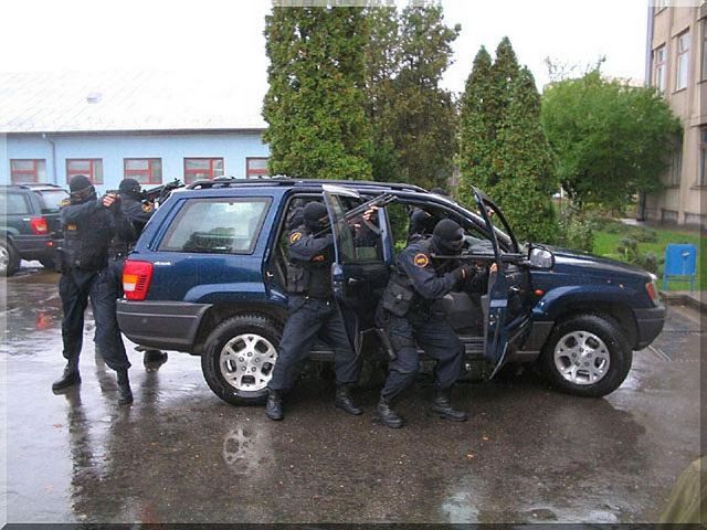 Blue Jeep Grand Cherokee with police officers exiting and aiming weapons. Another Jeep is visible behind it