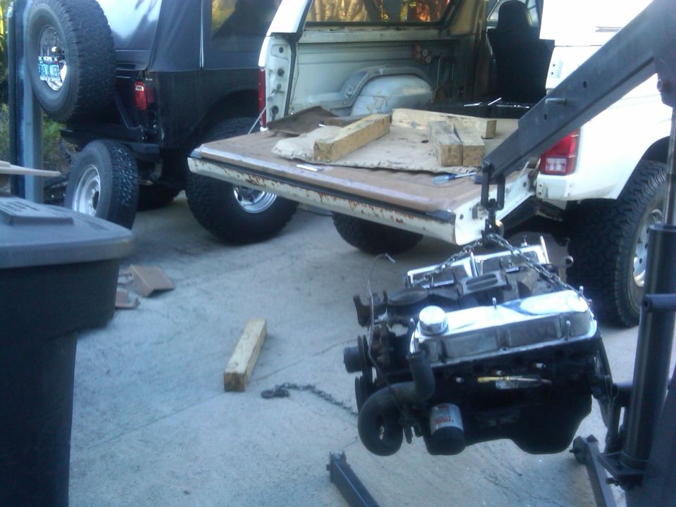 Engine suspended by a crane, with the tailgate of a light-colored truck open