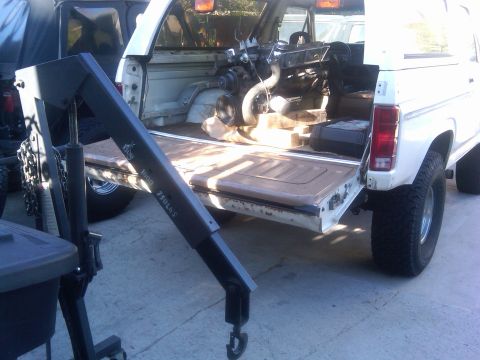 1986 Ford Bronco - A white 1986 Ford Bronco is shown with its engine removed and an engine hoist positioned in the cargo area. The hoist has visible weight ra…