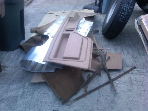 1986 Ford Bronco - Disassembled car interior parts are scattered on the ground, with a tire and trash can visible in the background.