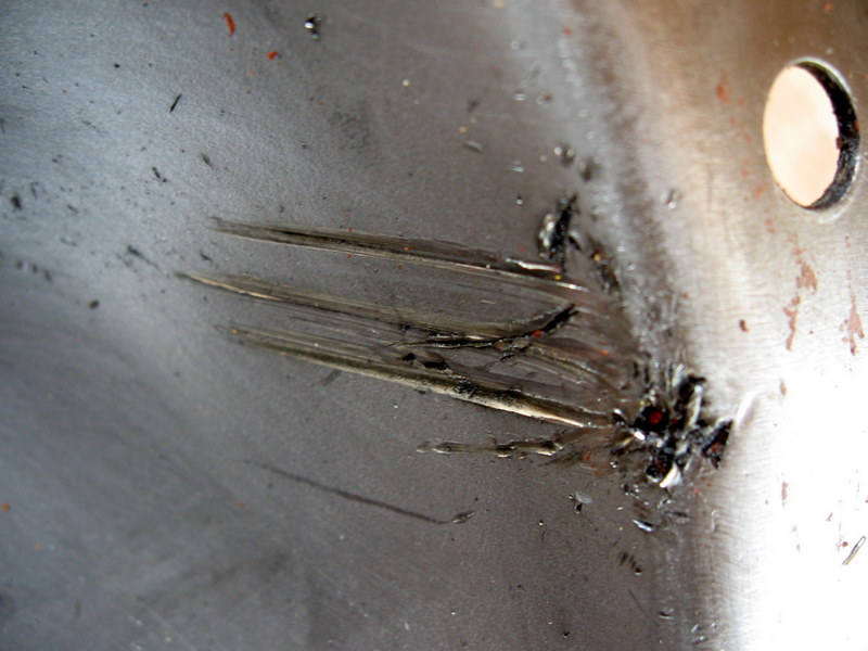 Close-up of a scratched and dented metal surface with a circular hole