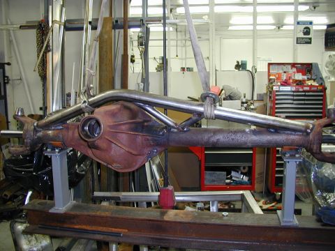 1979 Ford Bronco - A rusty rear axle assembly with added metal tubing is being worked on in a garage setting.