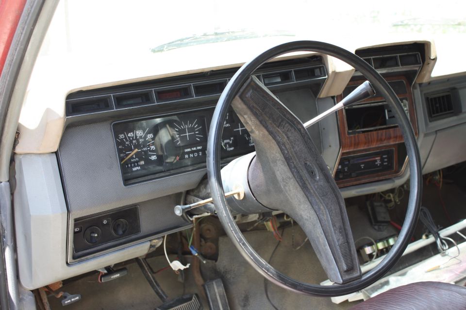 Dashboard of a 1980s Ford truck with a large steering wheel and analog gauges. Wood grain trim is visible
