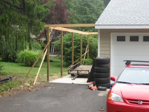 1996 Ford Bronco - A red sedan is parked in front of a garage with a partially built wooden structure in the background.