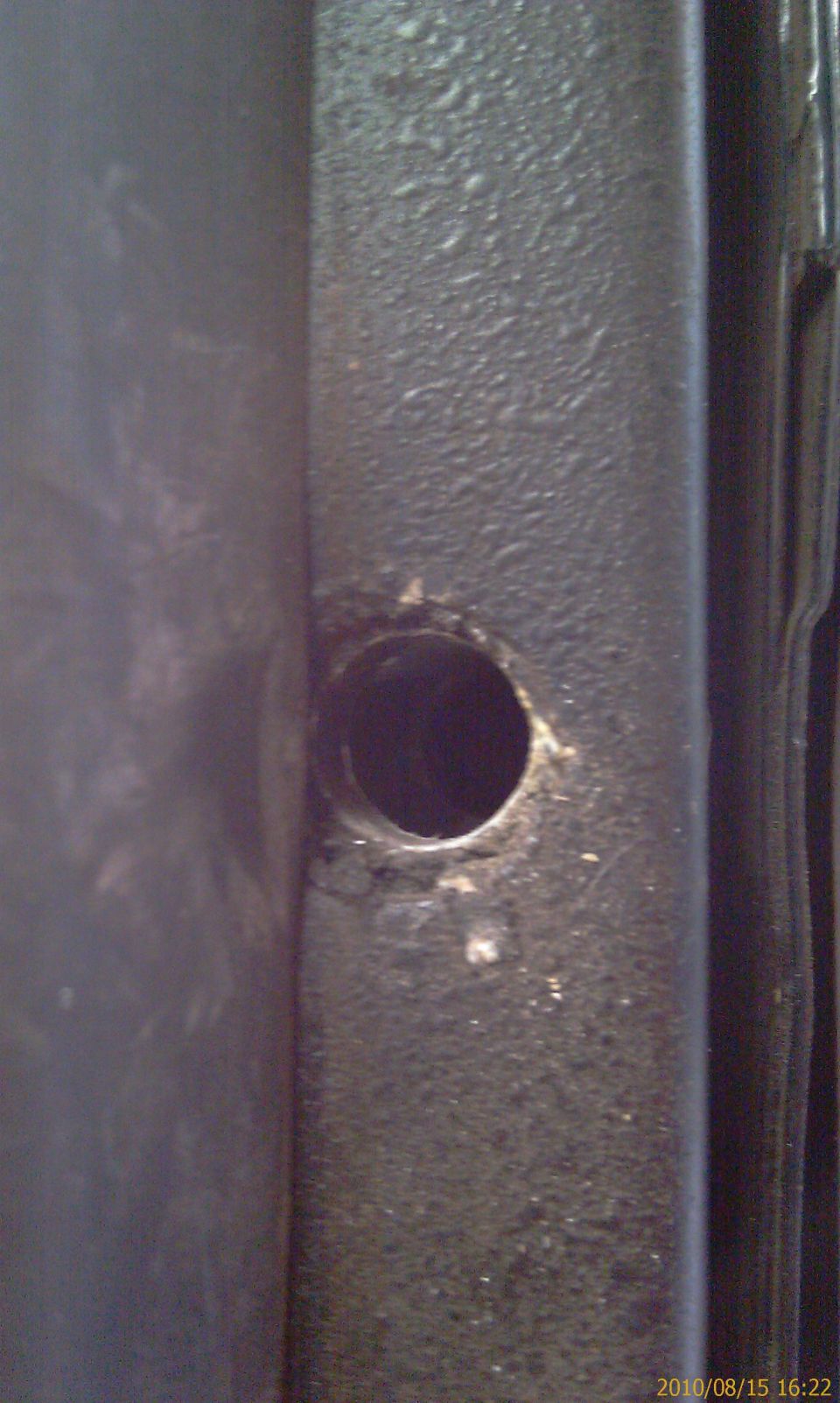 Close-up of a dark, textured metal frame with a circular hole and some white debris