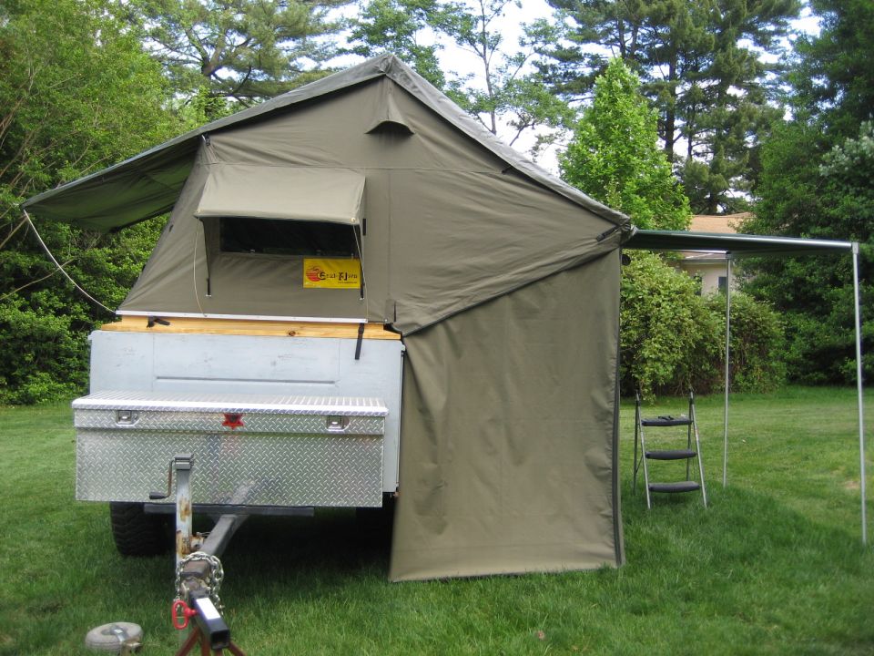 Tent trailer with a diamond plate toolbox mounted on the front, set up on a grassy area