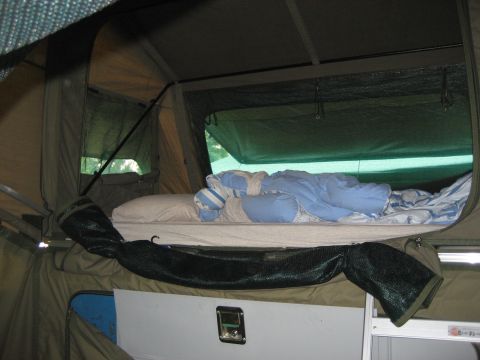 1996 Ford Bronco - View inside a pop-up camper showing a bed with pillows and blankets, ready for use.