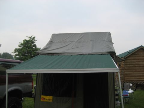 1996 Ford Bronco - Truck with an attached camper tent, parked near a wooden building.