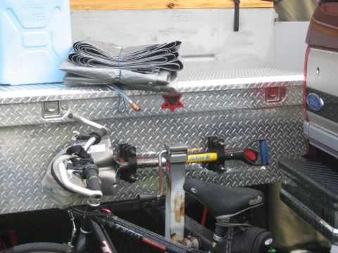 1996 Ford Bronco - Contents of a truck bed including a water jug, tarp, toolbox, and bicycle, with tools secured.