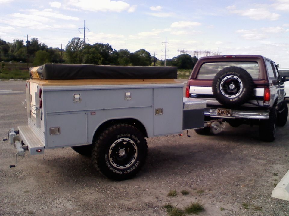 Gray off-road camper trailer with rooftop tent hitched to maroon and silver Ford Bronco