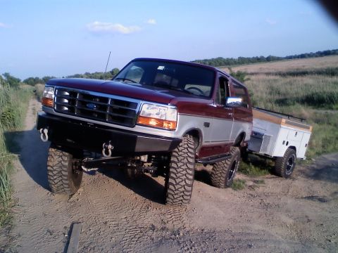 1996 Ford Bronco - A lifted 1996 Ford Bronco tows a trailer through a grassy field under a clear sky.