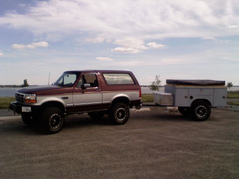 1996 Ford Bronco - A two-tone 1996 Ford Bronco is seen from the side, hitched to a utility trailer near a body of water.