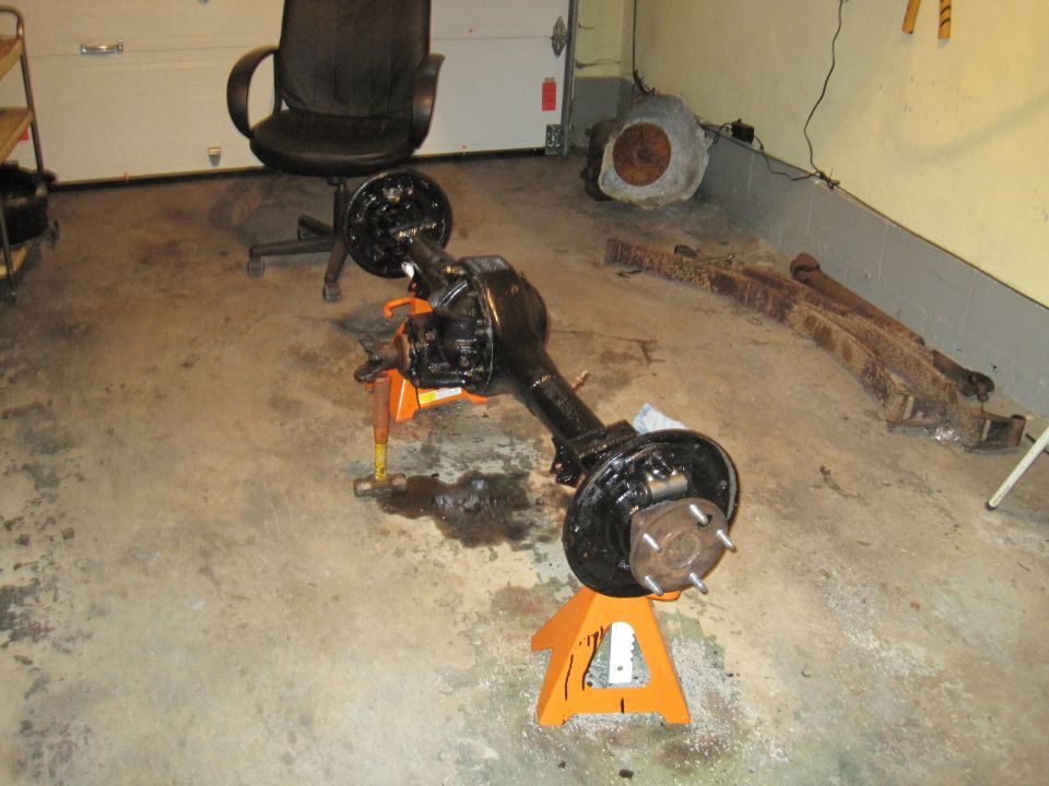 Rear axle assembly on orange jack stands, with leaf springs in background