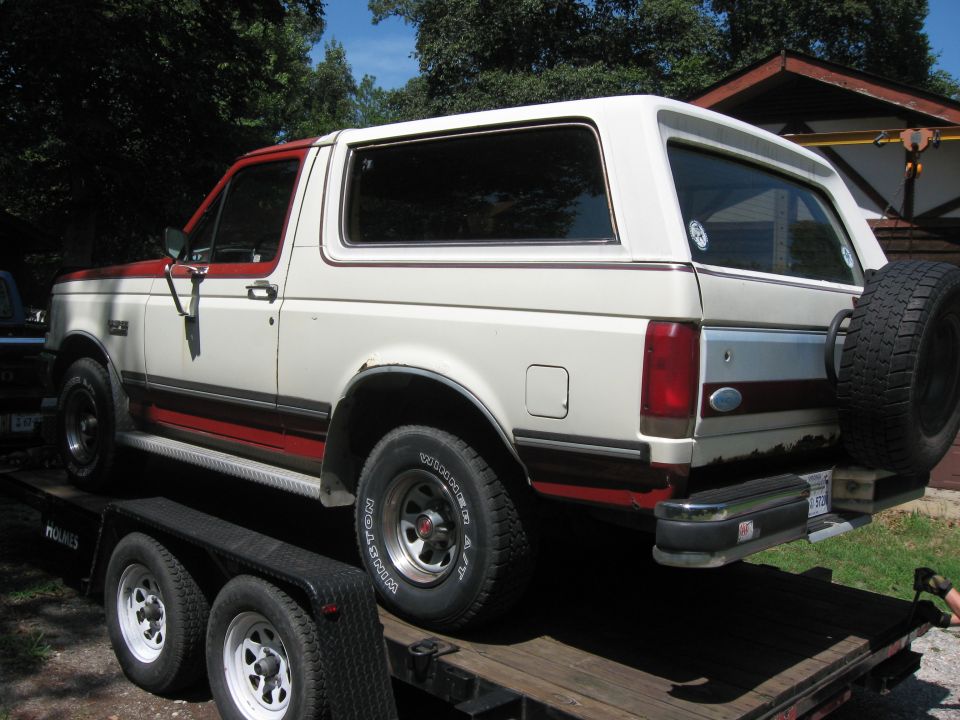 White and red Ford Bronco on a trailer, spare tire mounted on the back