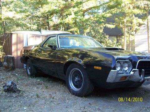 1972 Ford Ranchero - A black 1972 Ford Ranchero pickup truck is seen parked in a yard with trees and a shed in the background.