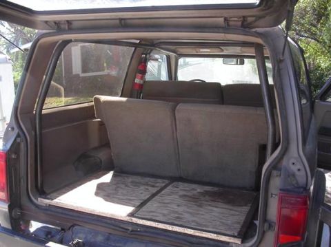 1990 Ford Bronco II - The rear cargo area of an SUV shows folded seats and a plywood floor, with a fire extinguisher mounted on the side.