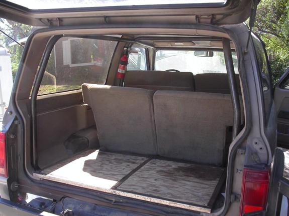 Rear cargo area of a compact SUV with plywood floor, folded tan seats and fire extinguisher