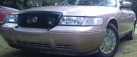 2000 Mercury Grand Marquis - The front of a gold Mercury Grand Marquis is shown parked outdoors on a grassy area.